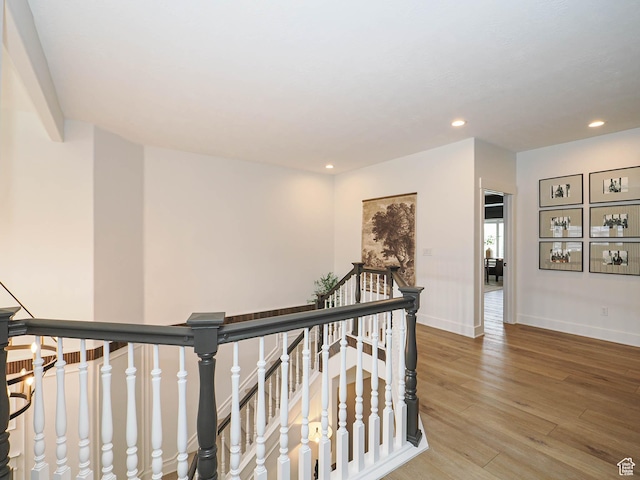 corridor with an upstairs landing, wood finished floors, recessed lighting, and baseboards