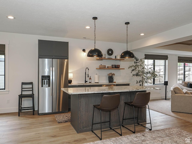 kitchen featuring stainless steel refrigerator with ice dispenser, a center island, open floor plan, a breakfast bar area, and light wood-style flooring