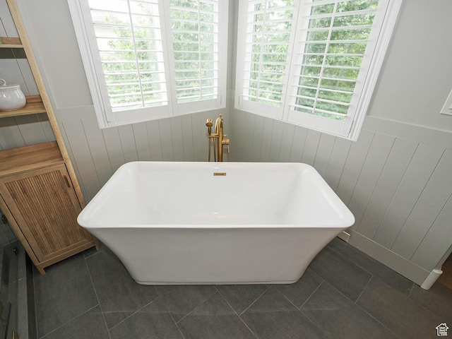 bathroom with plenty of natural light, a freestanding bath, tile patterned floors, and wainscoting