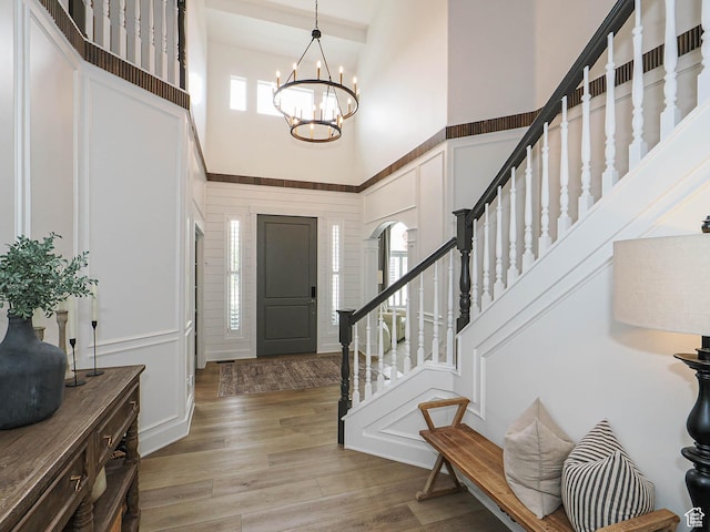 entrance foyer with a high ceiling, a decorative wall, a chandelier, stairway, and light wood-style floors