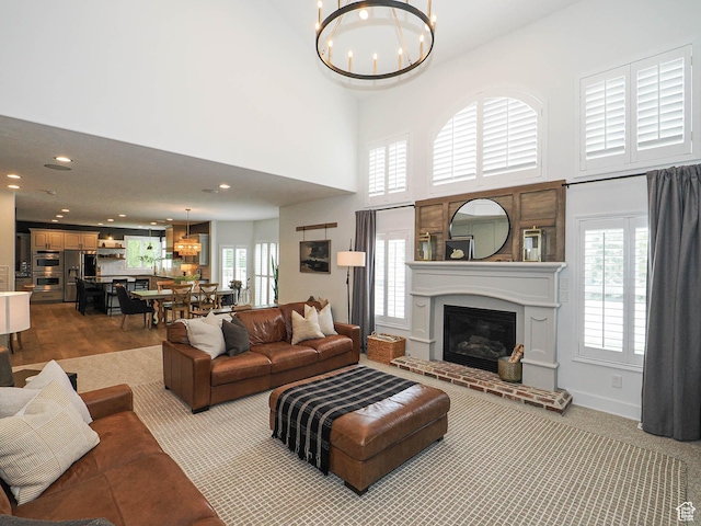 living area with a chandelier, a glass covered fireplace, recessed lighting, healthy amount of natural light, and a towering ceiling
