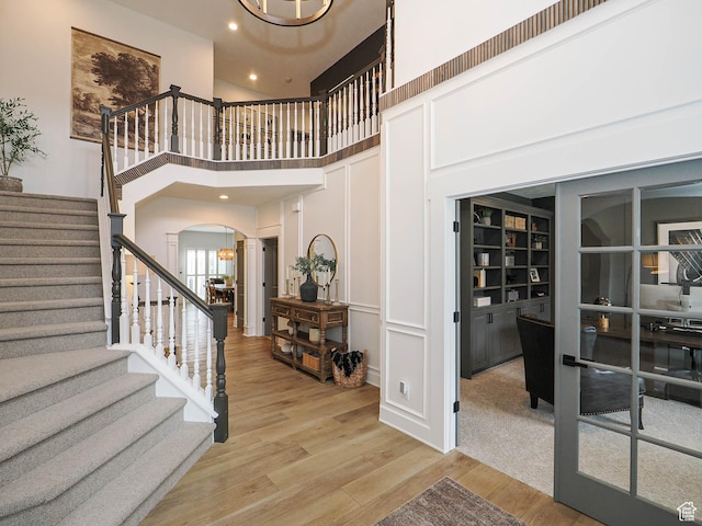 entrance foyer featuring arched walkways, light wood finished floors, stairs, a chandelier, and a towering ceiling