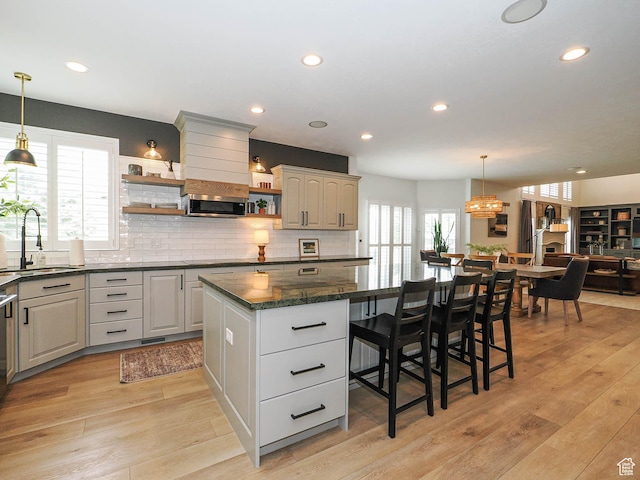 kitchen with a sink, open shelves, a kitchen island, stainless steel microwave, and light wood-style floors
