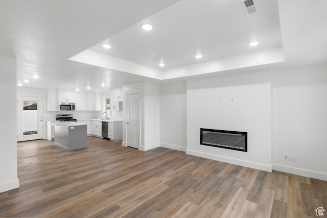 unfurnished living room with a tray ceiling, recessed lighting, baseboards, wood finished floors, and a glass covered fireplace
