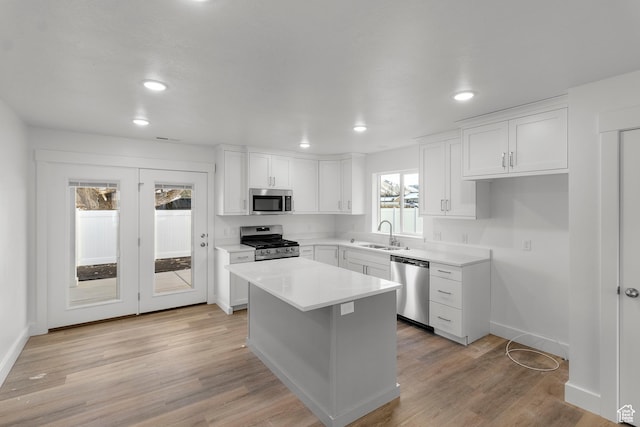 kitchen featuring stainless steel appliances, a sink, white cabinetry, a kitchen island, and light countertops