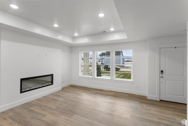 unfurnished living room with baseboards, a glass covered fireplace, light wood-style floors, and recessed lighting