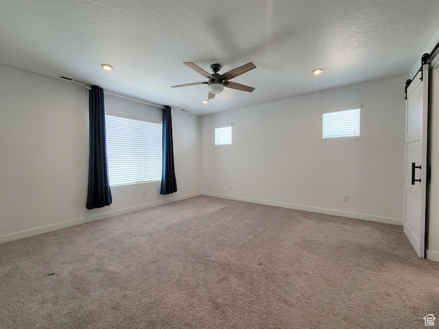 empty room with a barn door, ceiling fan, plenty of natural light, light carpet, and recessed lighting