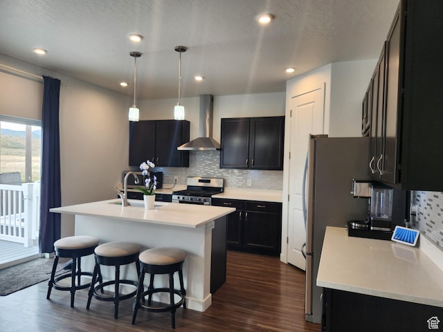 kitchen featuring wall chimney range hood, appliances with stainless steel finishes, a sink, backsplash, and dark wood-style flooring