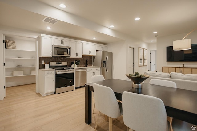 kitchen with stainless steel appliances, white cabinets, light wood finished floors, recessed lighting, and tasteful backsplash