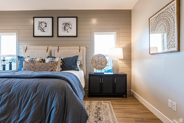 bedroom with wood walls, wood finished floors, and baseboards
