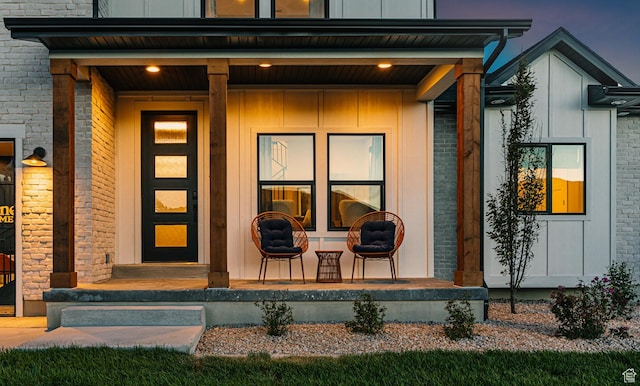 view of exterior entry featuring a porch, board and batten siding, and brick siding