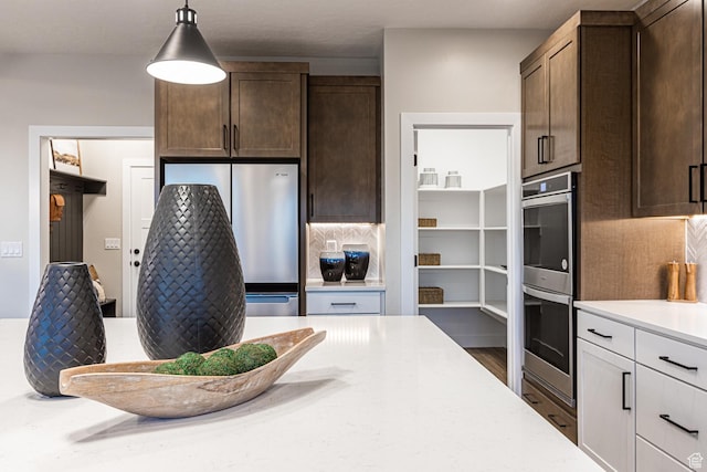 kitchen featuring appliances with stainless steel finishes, dark brown cabinets, decorative backsplash, and decorative light fixtures