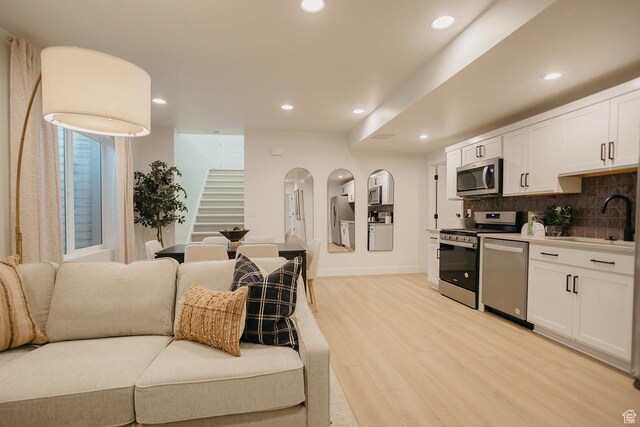 kitchen featuring appliances with stainless steel finishes, a sink, light wood finished floors, white cabinets, and decorative backsplash