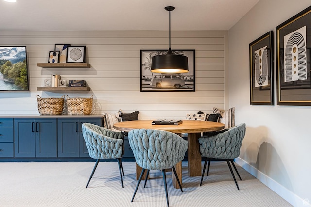 dining space with light carpet, baseboards, and wood walls