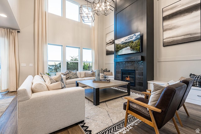 living area featuring a towering ceiling, wood finished floors, a tiled fireplace, and a chandelier