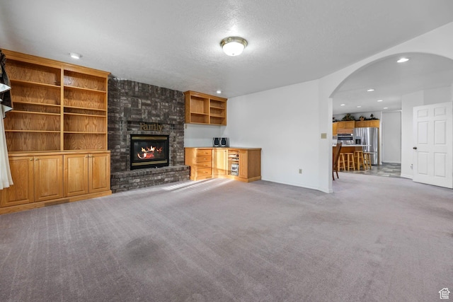 unfurnished living room with arched walkways, carpet, a fireplace, a textured ceiling, and recessed lighting