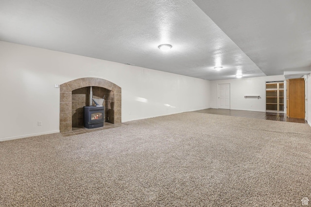 finished below grade area featuring a wood stove, baseboards, carpet floors, and a textured ceiling