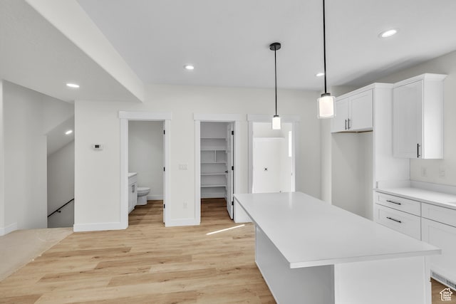 kitchen with light countertops, light wood finished floors, white cabinetry, a center island, and pendant lighting