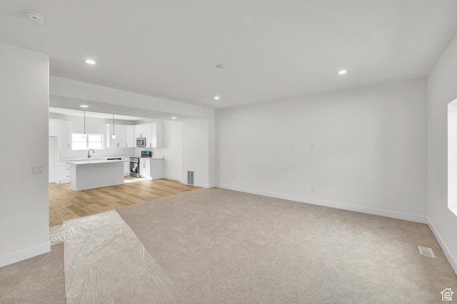 unfurnished living room featuring light carpet, baseboards, a sink, recessed lighting, and light wood-type flooring