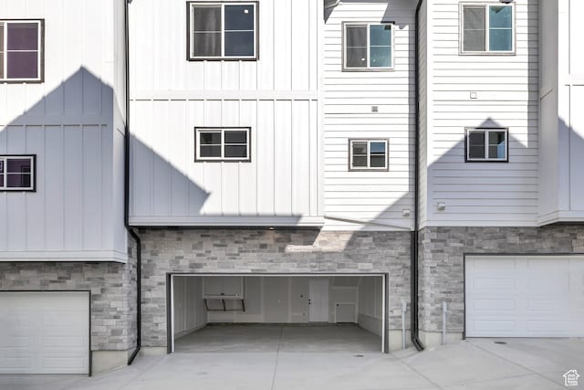 view of home's exterior with stone siding, a garage, board and batten siding, and driveway