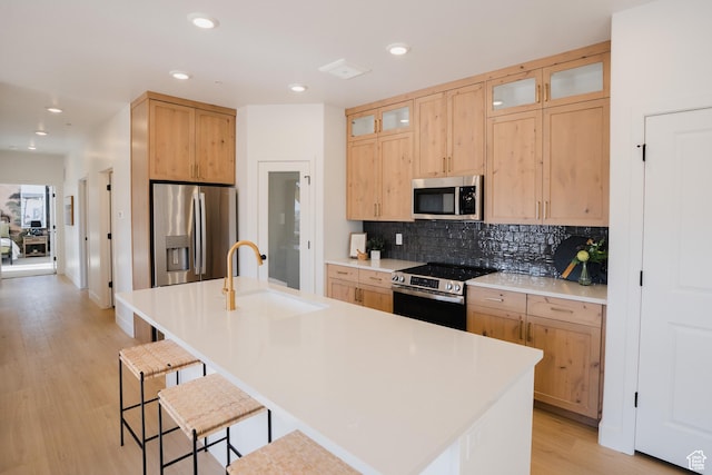 kitchen featuring appliances with stainless steel finishes, a sink, light brown cabinets, a breakfast bar, and backsplash