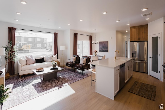 kitchen featuring appliances with stainless steel finishes, a sink, open floor plan, light wood finished floors, and recessed lighting
