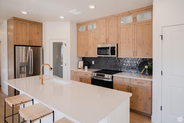 kitchen with a sink, stainless steel appliances, a kitchen breakfast bar, decorative backsplash, and glass insert cabinets