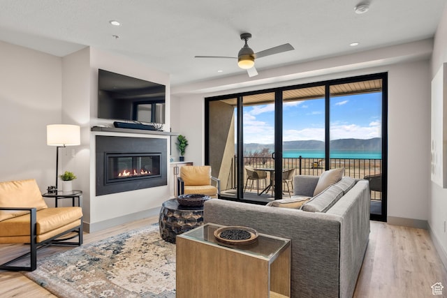 living room with a glass covered fireplace, wood finished floors, a ceiling fan, baseboards, and recessed lighting
