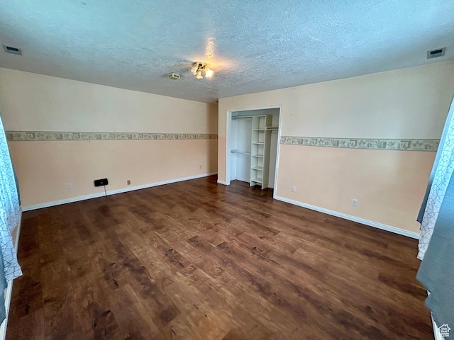 unfurnished bedroom with dark wood-style floors, a textured ceiling, baseboards, and a closet