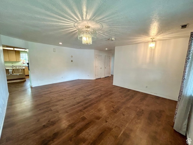 unfurnished room with a chandelier, dark wood-style flooring, a textured ceiling, and baseboards