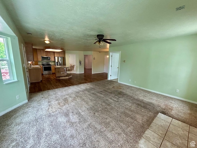 unfurnished living room featuring dark carpet, baseboards, a textured ceiling, and a ceiling fan
