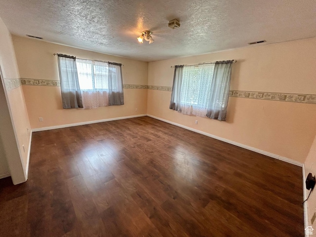 spare room featuring a textured ceiling, dark wood finished floors, and baseboards