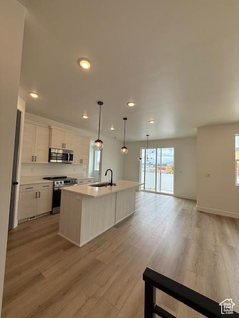 kitchen with appliances with stainless steel finishes, a sink, light wood-style flooring, an island with sink, and recessed lighting