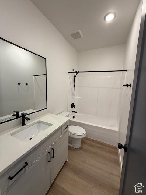 full bath with bathing tub / shower combination, vanity, wood finished floors, and toilet