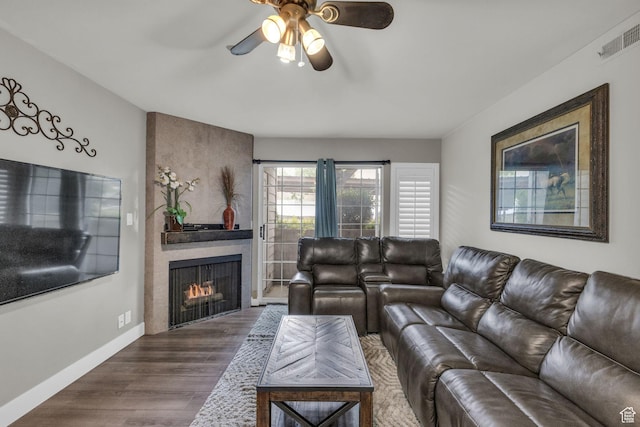living area featuring a ceiling fan, wood finished floors, a large fireplace, and baseboards