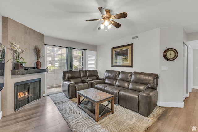 living area featuring wood finished floors, a ceiling fan, a warm lit fireplace, and baseboards