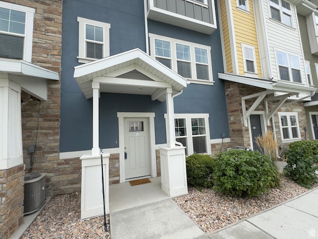 entrance to property with stone siding, cooling unit, and stucco siding