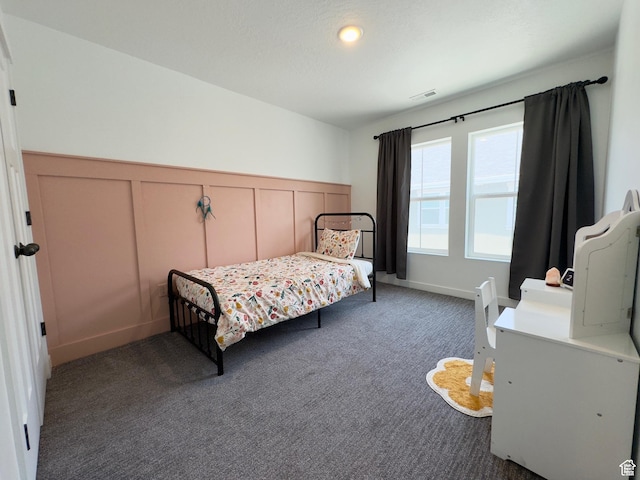 carpeted bedroom featuring a decorative wall and wainscoting