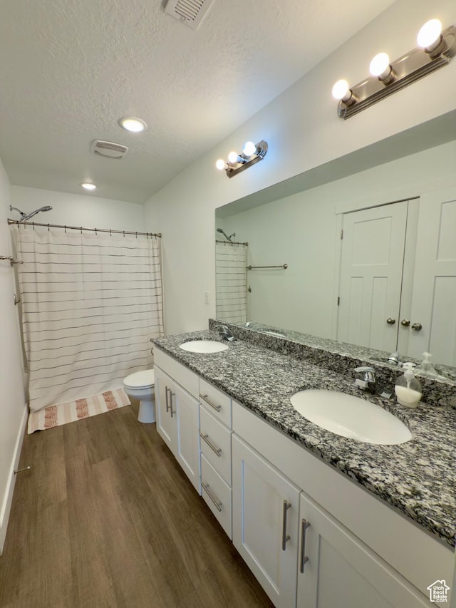 full bath featuring wood finished floors, a textured ceiling, toilet, double vanity, and curtained shower