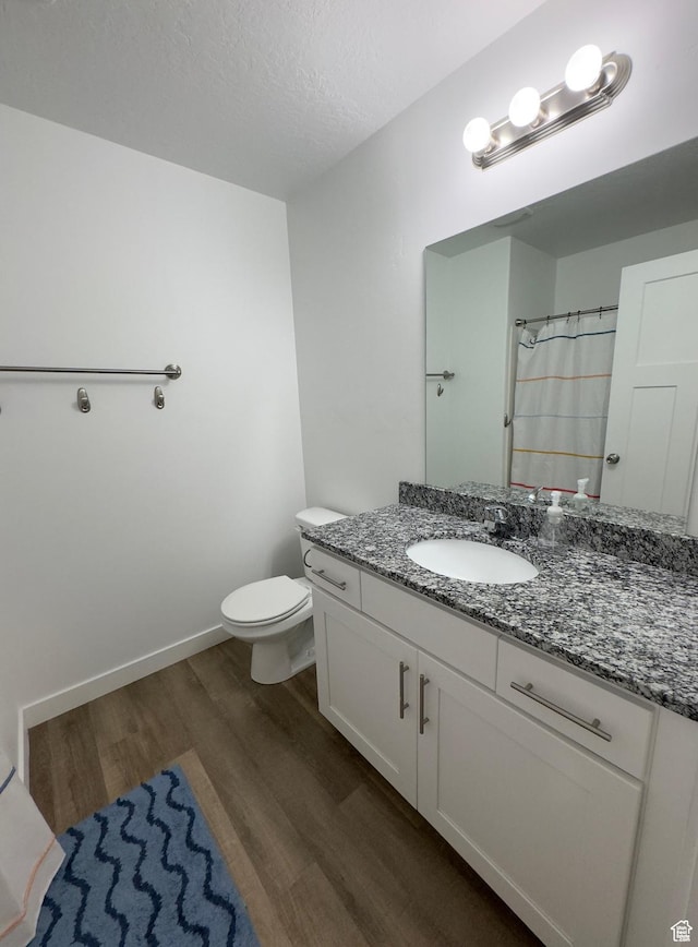 bathroom featuring wood finished floors, vanity, toilet, baseboards, and a textured ceiling