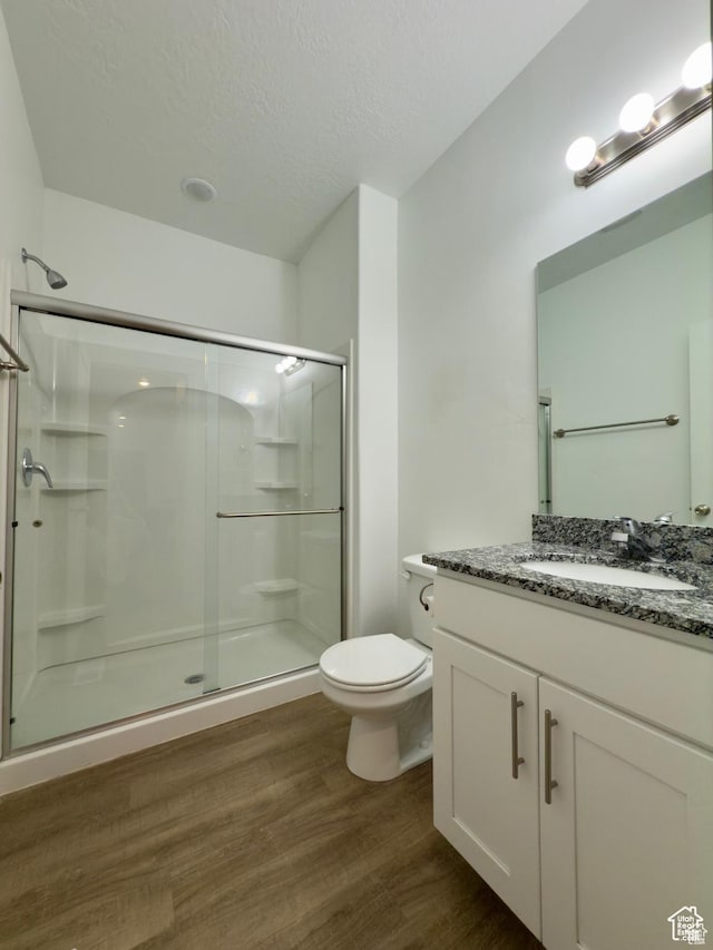 full bathroom featuring a shower stall, wood finished floors, toilet, vanity, and a textured ceiling