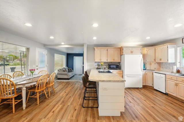 kitchen featuring white appliances, light brown cabinetry, decorative backsplash, recessed lighting, and a kitchen breakfast bar