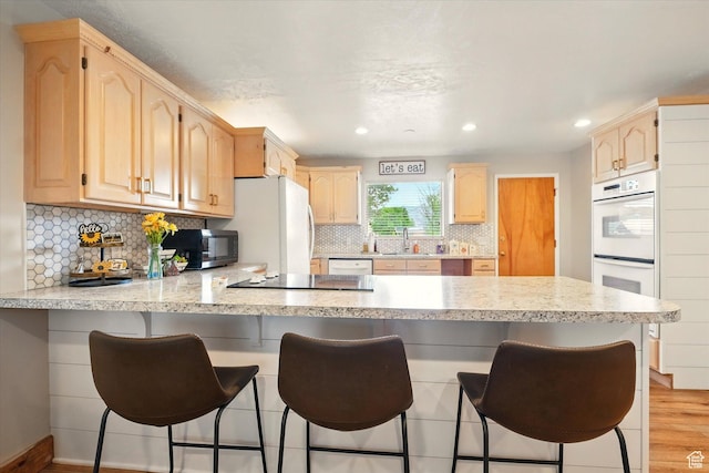 kitchen featuring a peninsula, black appliances, light brown cabinetry, a sink, and light wood-type flooring