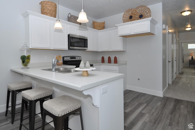 kitchen featuring stainless steel appliances, a peninsula, white cabinetry, a kitchen breakfast bar, and dark wood-type flooring