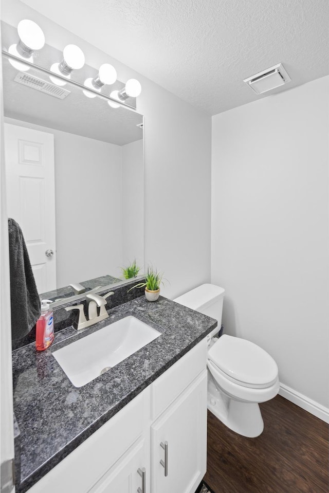 half bathroom featuring wood finished floors, vanity, toilet, a textured ceiling, and baseboards