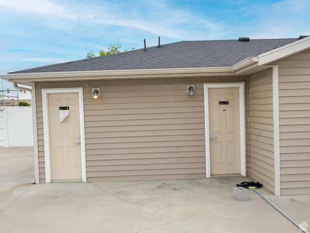 view of exterior entry with a shingled roof, a patio area, and fence