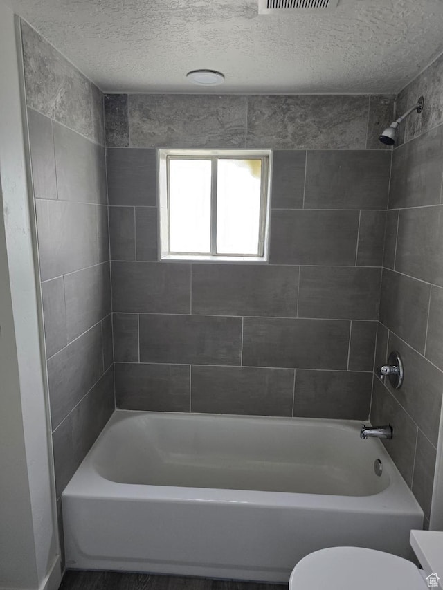 bathroom with toilet, shower / tub combination, and a textured ceiling
