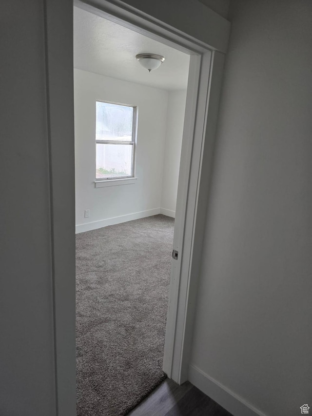unfurnished room with baseboards and dark carpet