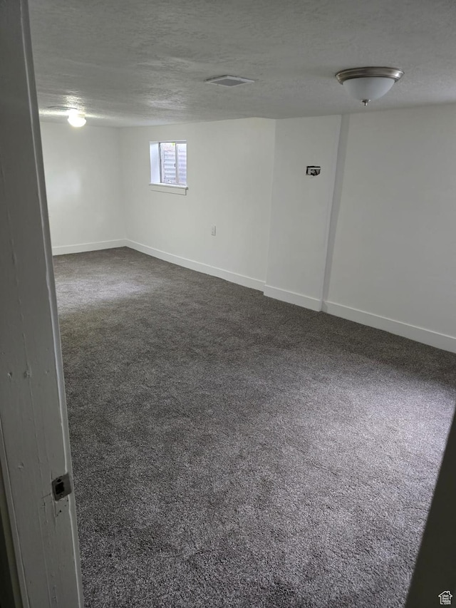 basement featuring dark carpet, baseboards, and a textured ceiling