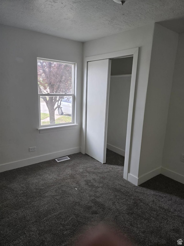 unfurnished bedroom featuring dark colored carpet, baseboards, a textured ceiling, and a closet